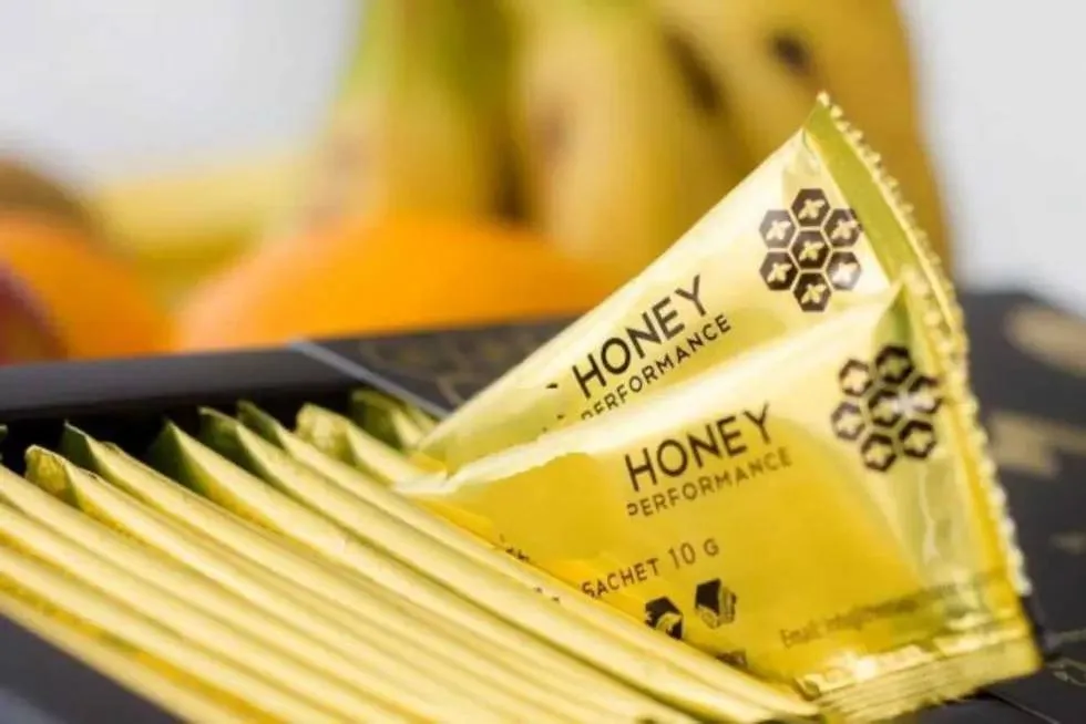 Sobres dorados del producto conocido como Miel del amor sobre una superficie, con una lupa que revela pastillas, simbolizando los fármacos ocultos.