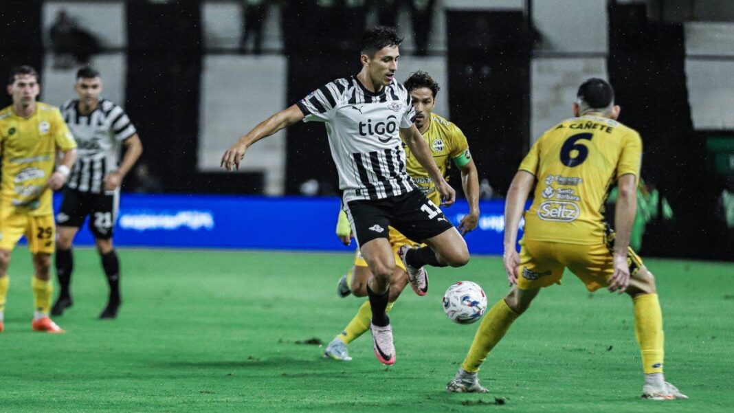 Escudo del Club Libertad de Paraguay sobre fondo de estadio de fútbol.