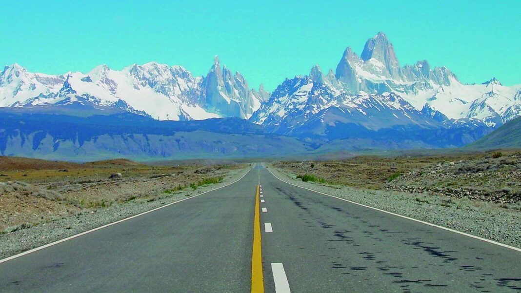 Persona consultando un dispositivo móvil para planificar un viaje, con maleta de fondo.