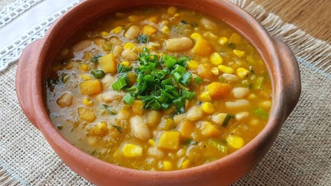 Plato de locro argentino con maíz, porotos y carne, servido en una cazuela de barro